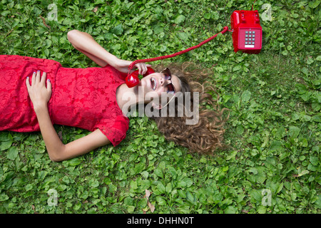 Teenage girl lying on grass holding téléphone rouge Banque D'Images