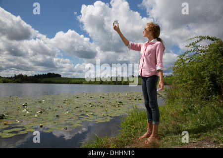 Teenage girl holding up bocal en verre à côté du lac Banque D'Images