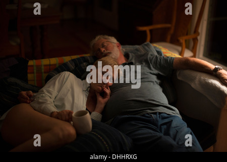 Senior couple reclining on sofa at night Banque D'Images