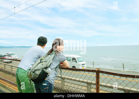 Jeune couple leaning against fence, regardant la mer Banque D'Images