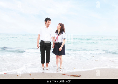 Young couple wearing school uniform standing on beach Banque D'Images