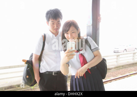 Jeune couple sur un quai de gare looking at smartphone Banque D'Images