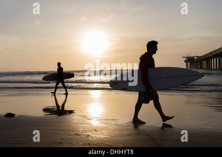 Deux hommes portant des planches sur la plage Banque D'Images