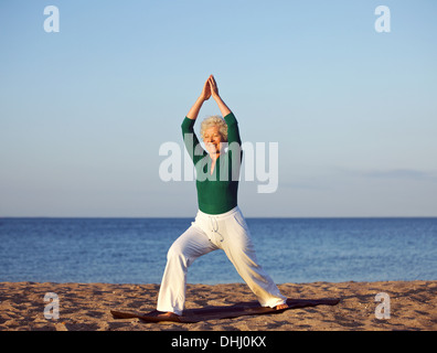 Senior woman stretching contre fond de plage. Mature Woman exercising on sandy beach in morning Banque D'Images