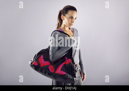Portrait de jeune femme fit transporter sac de sport à la recherche de là à copyspace sur fond gris. Belle femme de race blanche Banque D'Images