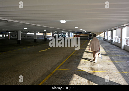 Sunlit Alone femme shopper marchant vers la sortie tenant sac à main dans le parking déserté de plusieurs étages Lakeside centre commercial West Thurrock Essex Angleterre Royaume-Uni Banque D'Images