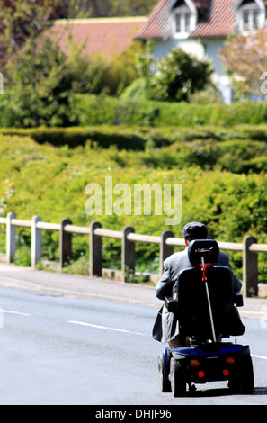 Vue arrière ou senior man riding scooter de mobilité sur route de campagne. Banque D'Images