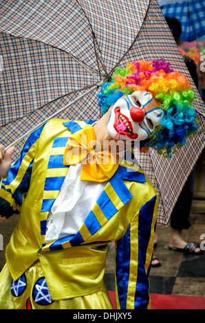 Un drôle de clown en costume complet, avec perruque de couleur vive, masque et l'enveloppe, qui souffle dans un sifflet. Banque D'Images