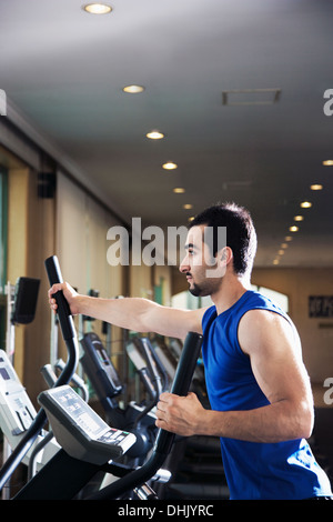 Jeune homme musclé exerçant sur un cross trainer dans la salle de sport Banque D'Images
