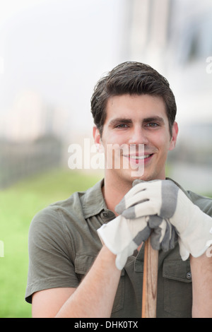 Portrait of young smiling man holding un râteau sur le toit d'un jardin dans la ville Banque D'Images