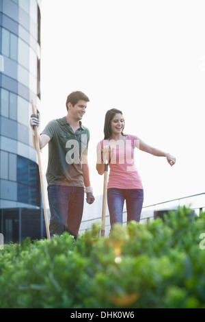 Deux jeunes gens souriants et jardinage pointant sur les plantes dans un jardin sur le toit dans la ville Banque D'Images