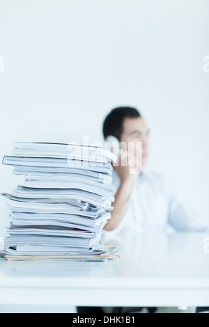 Homme d'affaires sur le téléphone avec une pile de papiers sur le bureau Banque D'Images