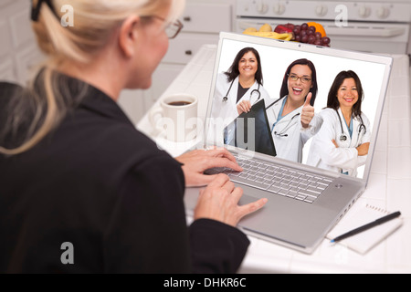 Femme assise dans la cuisine à l'aide de l'équipe de visualisation portable Hispanic Female médecins ou infirmières avec Thumbs Up Holding X-ray. Banque D'Images