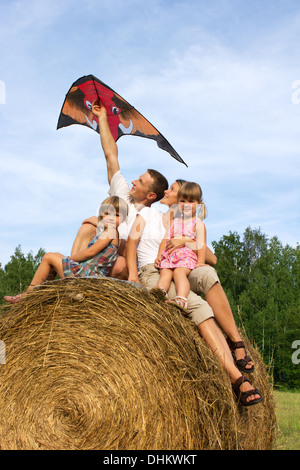 L'heureuse famille à cheval sur hay flying kite. Banque D'Images