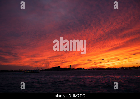 Coucher de soleil sur le port de New York, le 12 novembre 2013. Ellis Island est silhouetté contre le ciel. Banque D'Images