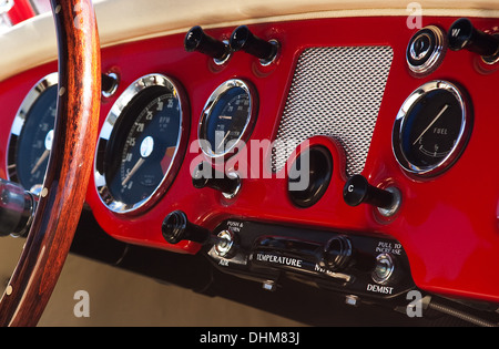 Ancienne voiture rouge tableau de bord avec une grande roue et plusieurs boutons et affichages mécaniques Banque D'Images