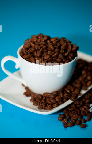 Les grains de café déborde d'une tasse, sur un fond bleu Banque D'Images