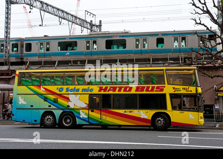 Un bus touristique Hato à deux étages coloré dans la rue tandis qu'un train passe derrière dans le centre de Tokyo, au Japon. Banque D'Images