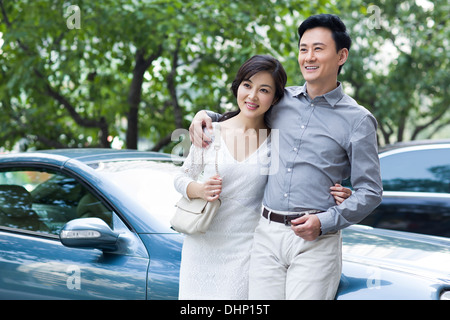 Heureux couple appuyé contre une nouvelle voiture Banque D'Images