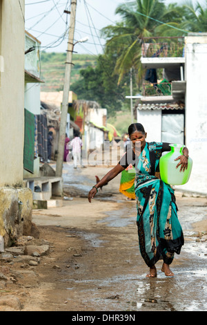 Personnes âgées femme indienne portant un pot d'eau en plastique d'un tube de mesure dans une rue village. L'Andhra Pradesh, Inde. Banque D'Images