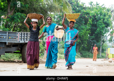 Happy smiling Indian Women et portant une cruche d'eau et des paniers dans une rue village. L'Andhra Pradesh, Inde Banque D'Images