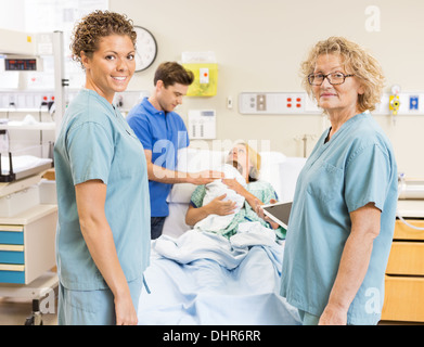 Smiling Nurses Standing contre Couple avec bébé en arrière-plan Banque D'Images
