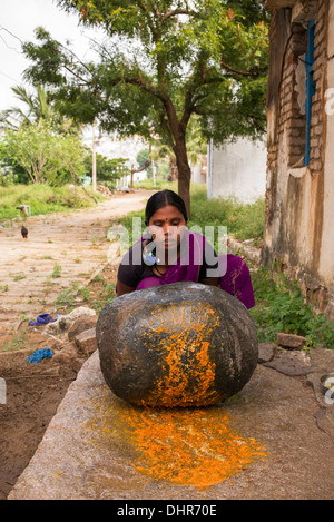 Femme indienne en utilisant une pierre pour moudre des ingrédients pour faire l'extérieur de son chutney maison de village rural. L'Andhra Pradesh, Inde Banque D'Images