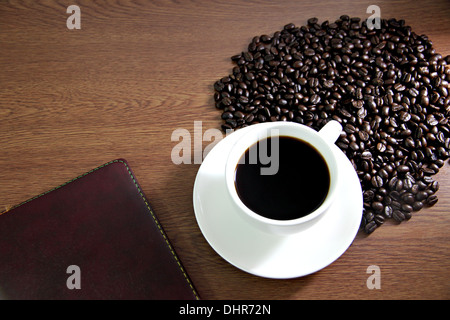 La photo Focus white tasse à café et livre sur la table de vieux bois près de les grains de café. Banque D'Images