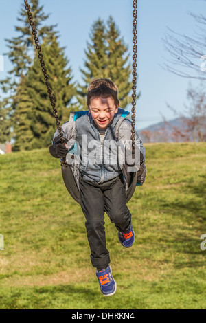 Parution du modèle, mignon, sourire, rire, garçon de 5 ans, de s'amuser dans l'aire de jeux en plein air, sur swing. Banque D'Images