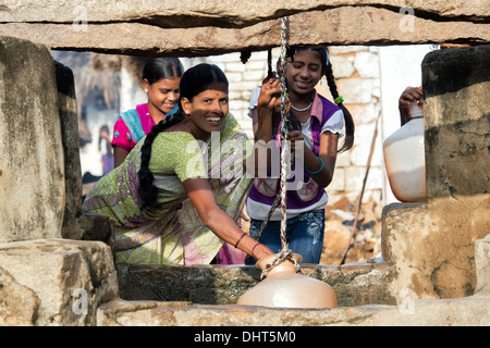 Femme indienne et les adolescentes dimensions de l'eau d'un puits dans un village-rue de l'Inde rurale. L'Andhra Pradesh, Inde Banque D'Images
