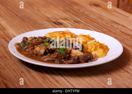 Goulasch de cerf avec des pommes et des pommes de terre sur la plaque avec fond de bois Banque D'Images