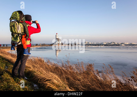 Pays-bas, Marken, lac Ijsselmeer. L'hiver. Het Paard phare appelé. Randonneur, femme avec enfant dans le dos prend photo Banque D'Images