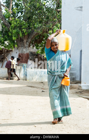 Personnes âgées femme indienne portant un pot en plastique avec de l'eau d'une pompe manuelle dans un village de l'Inde rurale. L'Andhra Pradesh, Inde Banque D'Images