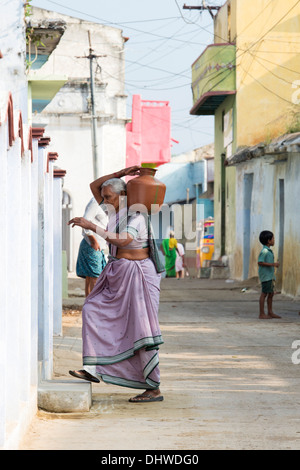 Personnes âgées femme indienne portant un pot en plastique avec de l'eau d'une borne fontaine dans son village house. L'Andhra Pradesh, Inde Banque D'Images