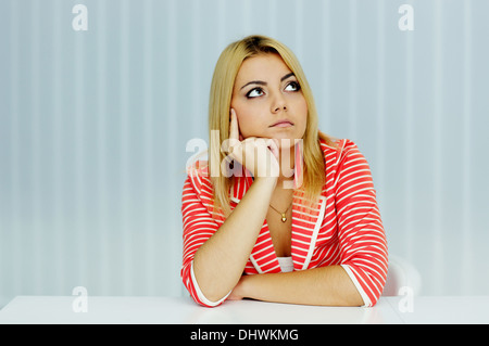 Jeune femme sérieuse en veste rouge assis à la table in office Banque D'Images