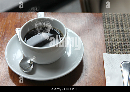 La photo sex café noir dans une tasse blanche sur la table et ont la fumée sortir. Banque D'Images