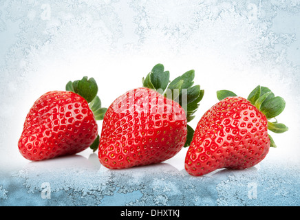 3 fraises fraîches jeter sur fond de glace bleu Banque D'Images