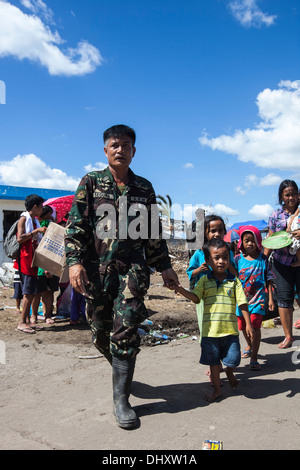 Un soldat avec l'armée philippine à la tête d'une famille à un aéronef de transport à Manille au champ Air Tacloban ici, 15 Novembre Banque D'Images