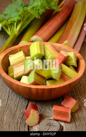Rhubarbe fraîche dans un bol en bois brun sur table de jardin Banque D'Images