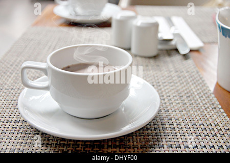 La photo sex café noir dans une tasse blanche sur la table et ont la fumée sortir. Banque D'Images