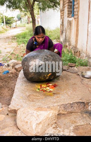 Femme indienne en utilisant une pierre pour moudre des ingrédients pour faire l'extérieur de son chutney maison de village rural. L'Andhra Pradesh, Inde Banque D'Images