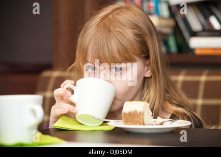 Petite fille blonde avec un gâteau de thé boissons Banque D'Images