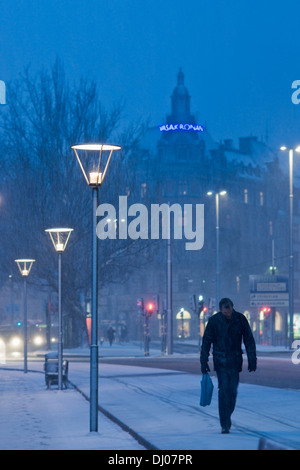 Homme avec tête penchée marche dans une tempête de neige par ville la nuit, Stockholm, Suède Banque D'Images