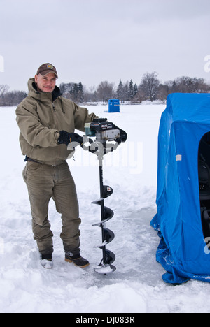 Homme tenant une tarière de forage dans la glace sur un lac gelé, Minneapolis, Minnesota, USA Banque D'Images