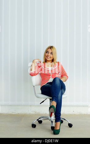 Jeune femme gaie assis sur la chaise et looking up Banque D'Images