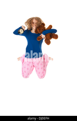 Jeune femme saute en bleu et rose pyjama avec réveil et ours en peluche Banque D'Images