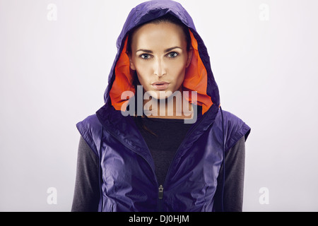 Portrait de belle jeune femme caucasienne dans une veste à capuchon sur fond gris. Femme Fitness Sportswear dans looking at camera Banque D'Images