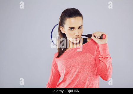 Portrait de jeune fille tenant une raquette de badminton à la caméra à contre fond gris. Banque D'Images