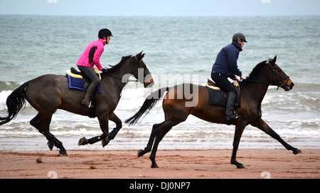 Deux chevaux avec cavaliers appréciant un galop le long Sands Paignton, Torbay, dans le Devon, Angleterre, Royaume-Uni Banque D'Images