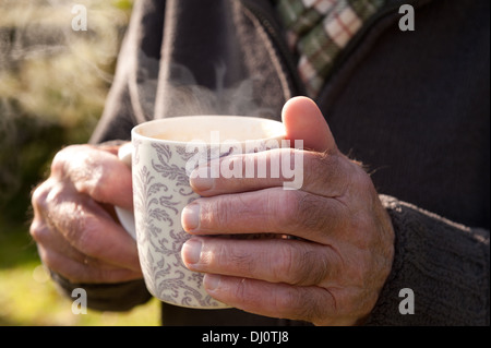 Réchauffer le froid les mains avec une tasse de thé chaud après le jardinage sur journée ensoleillée d'automne froid Banque D'Images